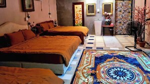 Habitación de hotel con dos camas, una zona de estar con mesa y sillas, un tapete decorativo y un ventanal con cortinas.