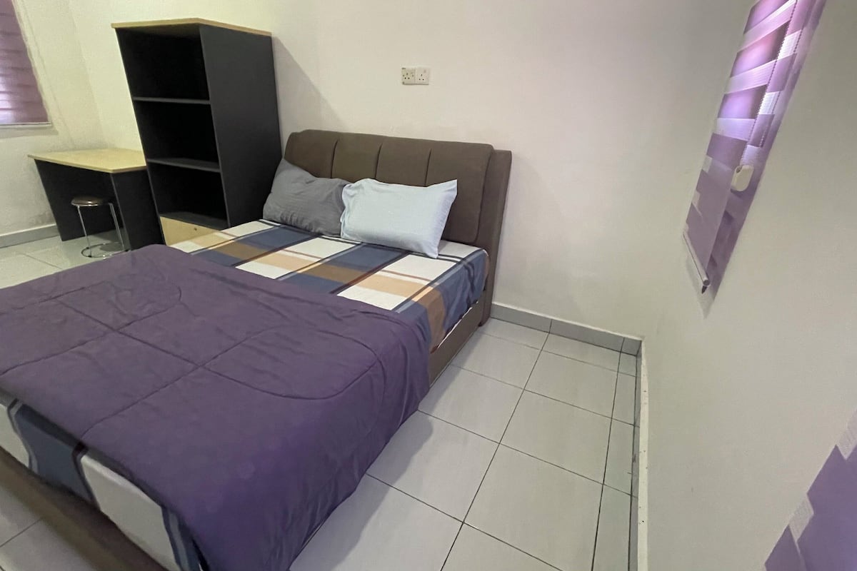 Ein Schlafzimmer mit Bett, Kleiderschrank, einem kleinen Tisch und einem Fenster mit Jalousien.