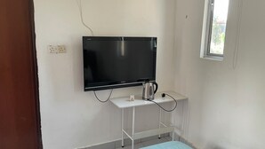 Una habitación con una televisión de pantalla plana montada en la pared, una mesita con una tetera y un ventanal.