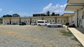A building with multiple rooms, a gravel parking area, and a few parked vehicles. - OYO 91026 M&H Hotel 2 (Bandar Penawar)