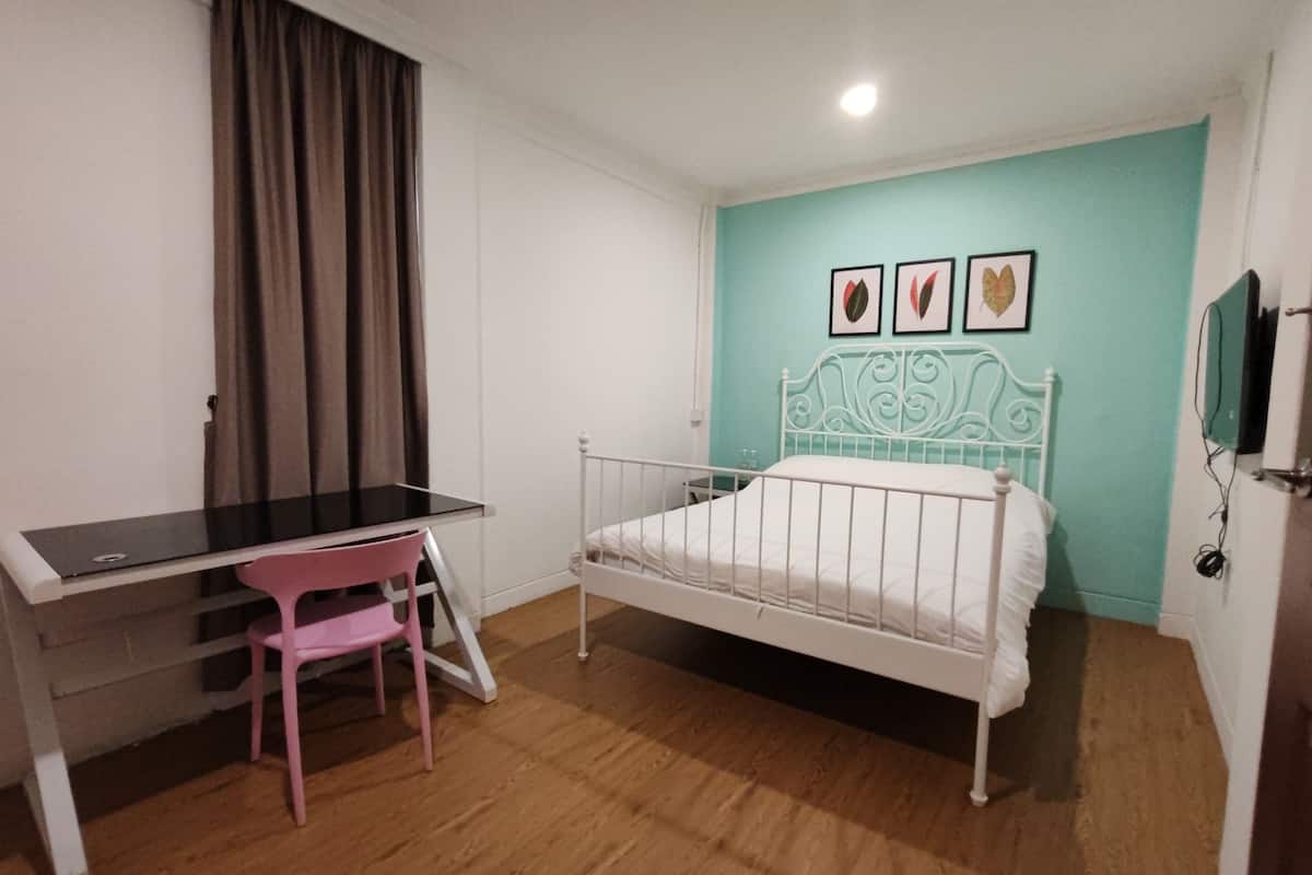 A bedroom with a bed, a desk, and a chair. There are three framed pictures on the wall.
