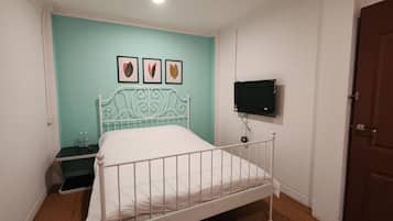 A bedroom with a white metal bed frame, a teal wall, and a mounted TV.