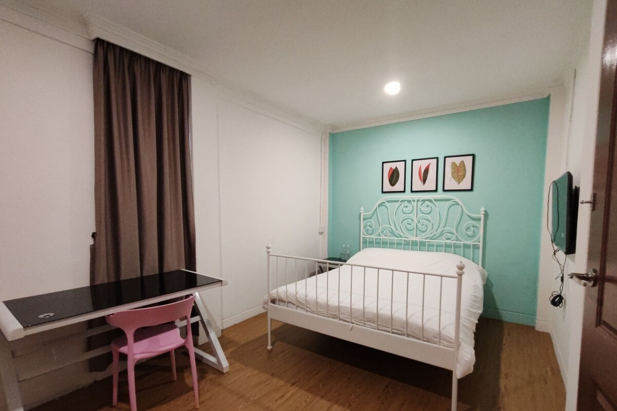 A bedroom with a bed, a desk, a chair, and a wall-mounted TV.