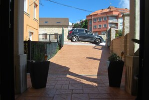 A paved driveway leading to a parked car, flanked by buildings and potted plants. - Casa Mariño (Goyanes)