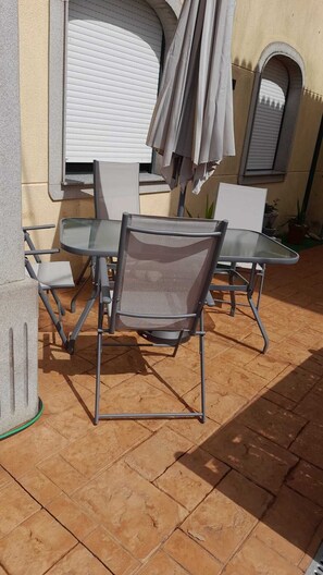 Un patio al aire libre con una mesa y sillas, un área de estar techada y piso de baldosas.