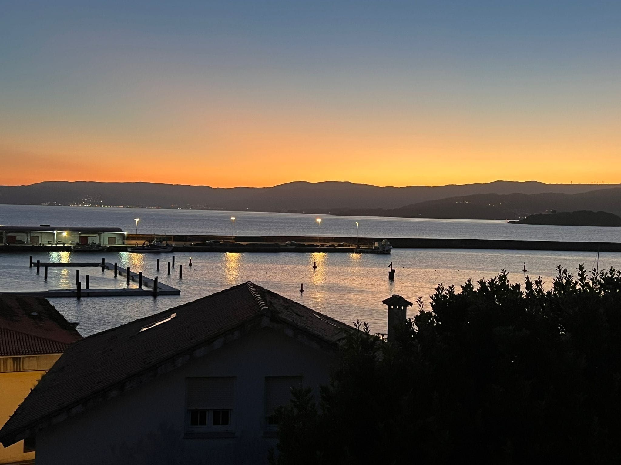 A coastal view with a pier extending into calm waters, a distant mountain range, and a clear sky.