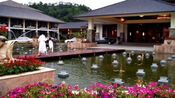 Un hotel con un elemento decorativo a base d'acqua in primo piano, diversi edifici e uno sfondo verdeggiante.