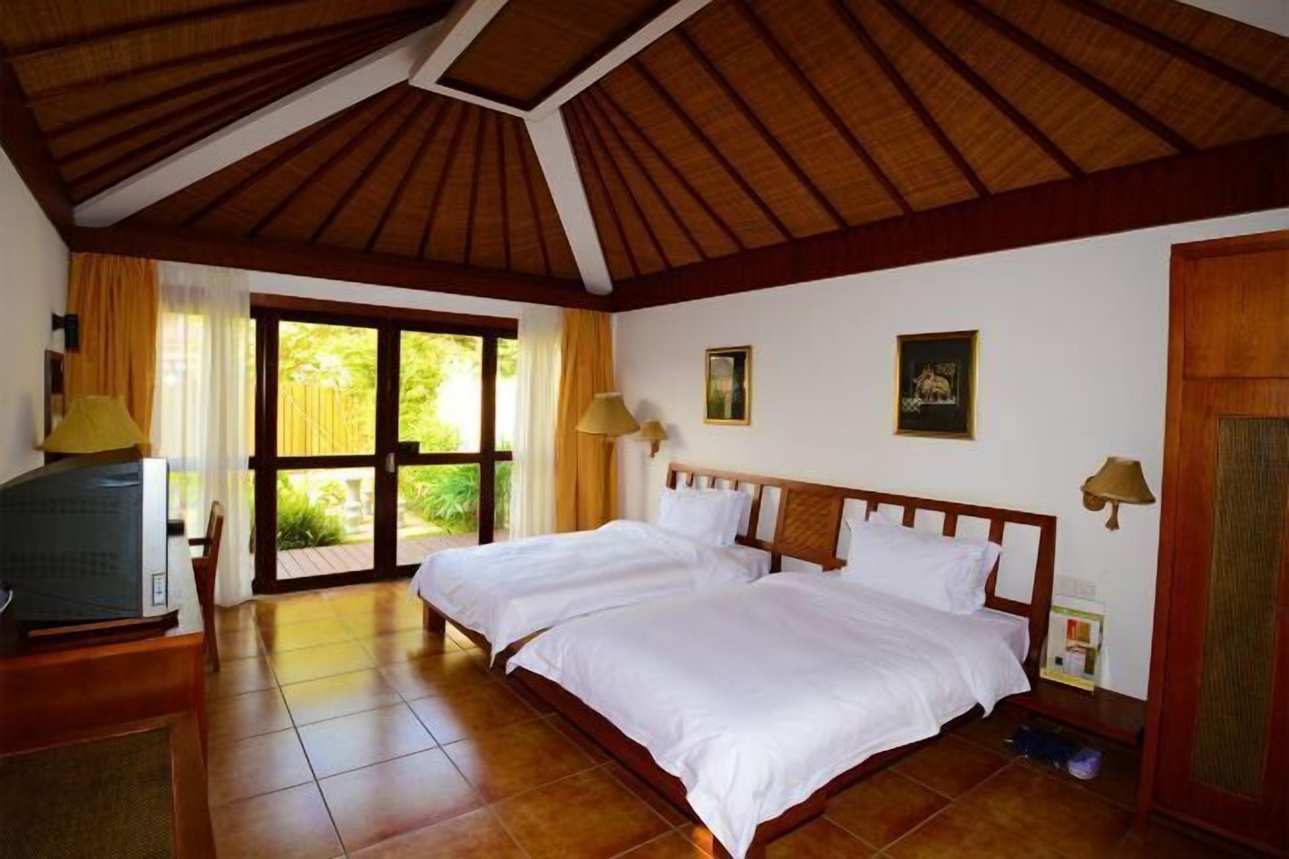 Una habitación con dos camas, televisión y una puerta corrediza de vidrio que da a un jardín.