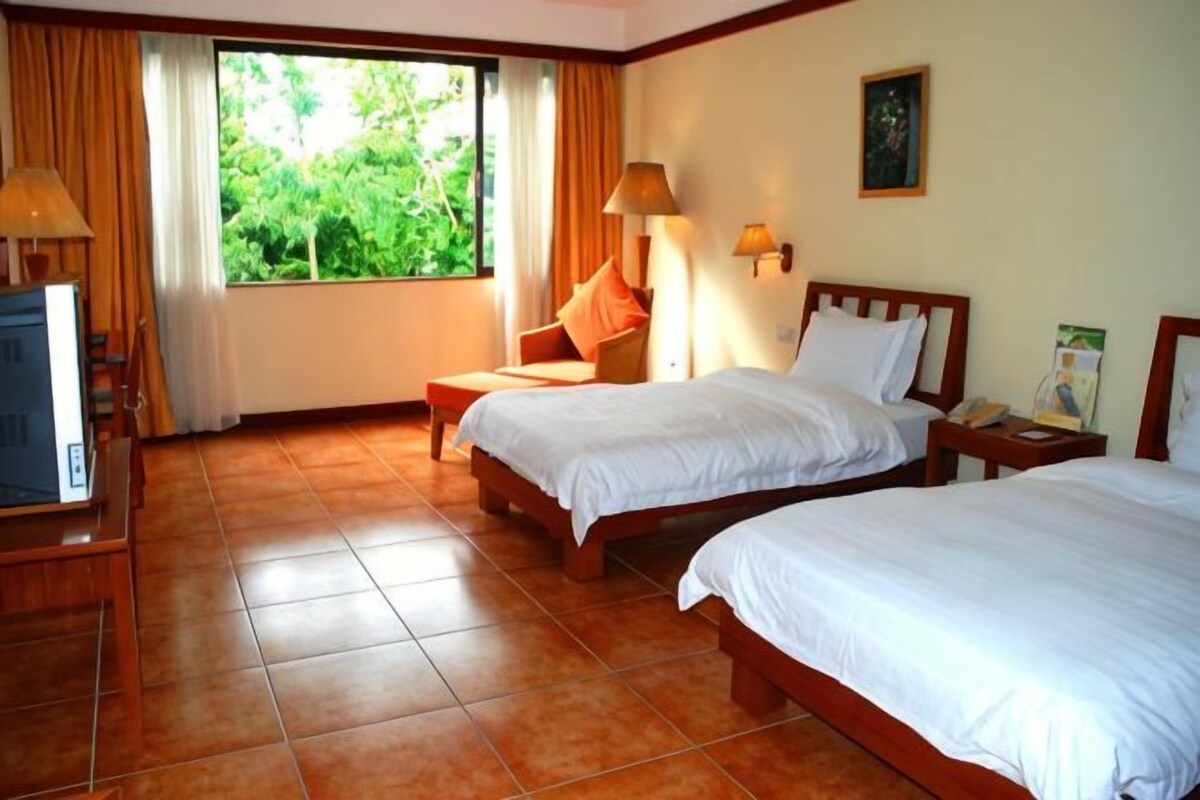 A hotel room with two beds, a desk, a chair, a TV, and a window with curtains.