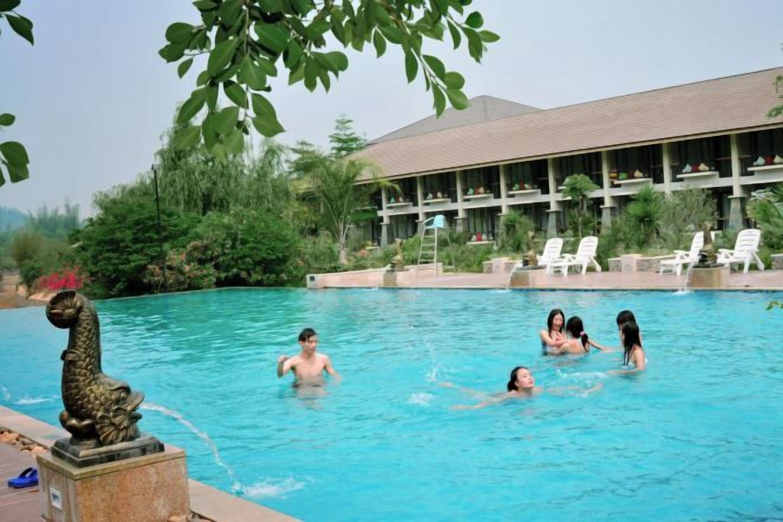A swimming pool with people, a statue, and a building with a roof and windows.