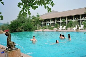 A swimming pool with people, a statue, and a building with a roof and windows.