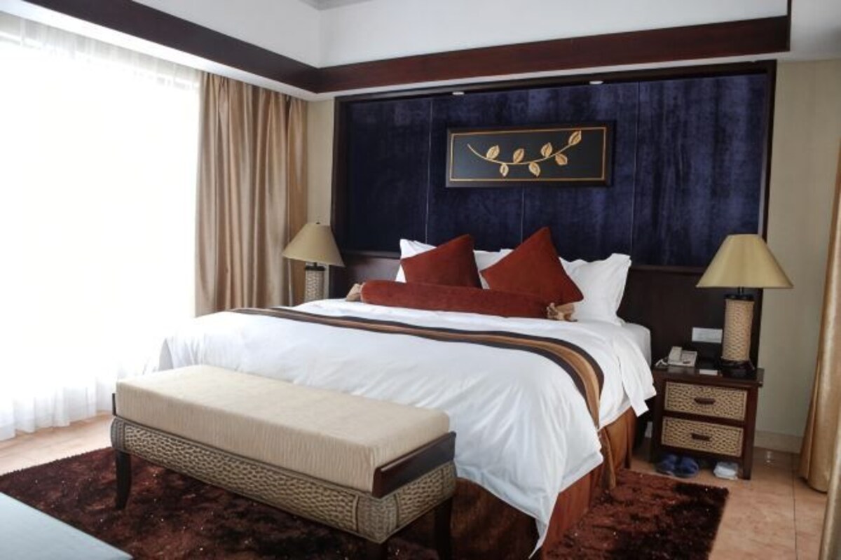 A hotel room with a large bed, bedside tables, a bench, and a view of the outdoors.