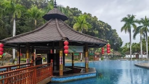 Un gazebo con tetto in tegole e lanterne rosse, circondato da una piscina e palme.