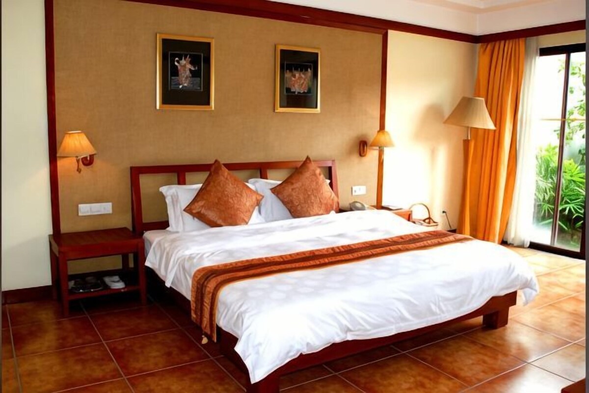 A hotel room with a large bed, two wall-mounted lamps, a nightstand, and a window with curtains.