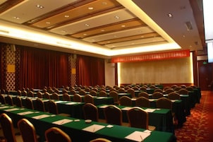 Un salón de conferencias con filas de mesas y sillas, suelo cubierto con alfombra roja y pared con diseño.