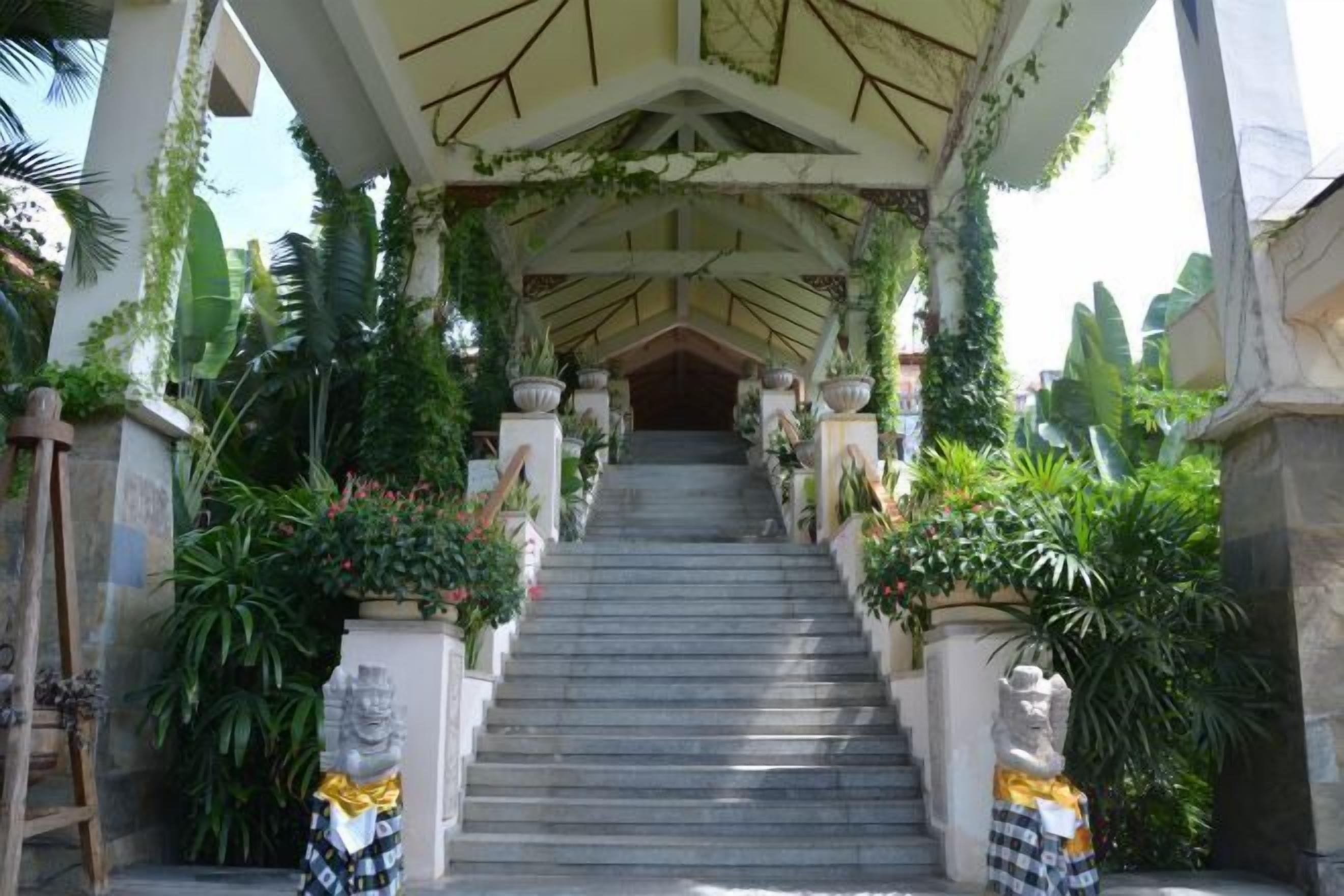 A staircase with a covered roof, flanked by potted plants and statues.