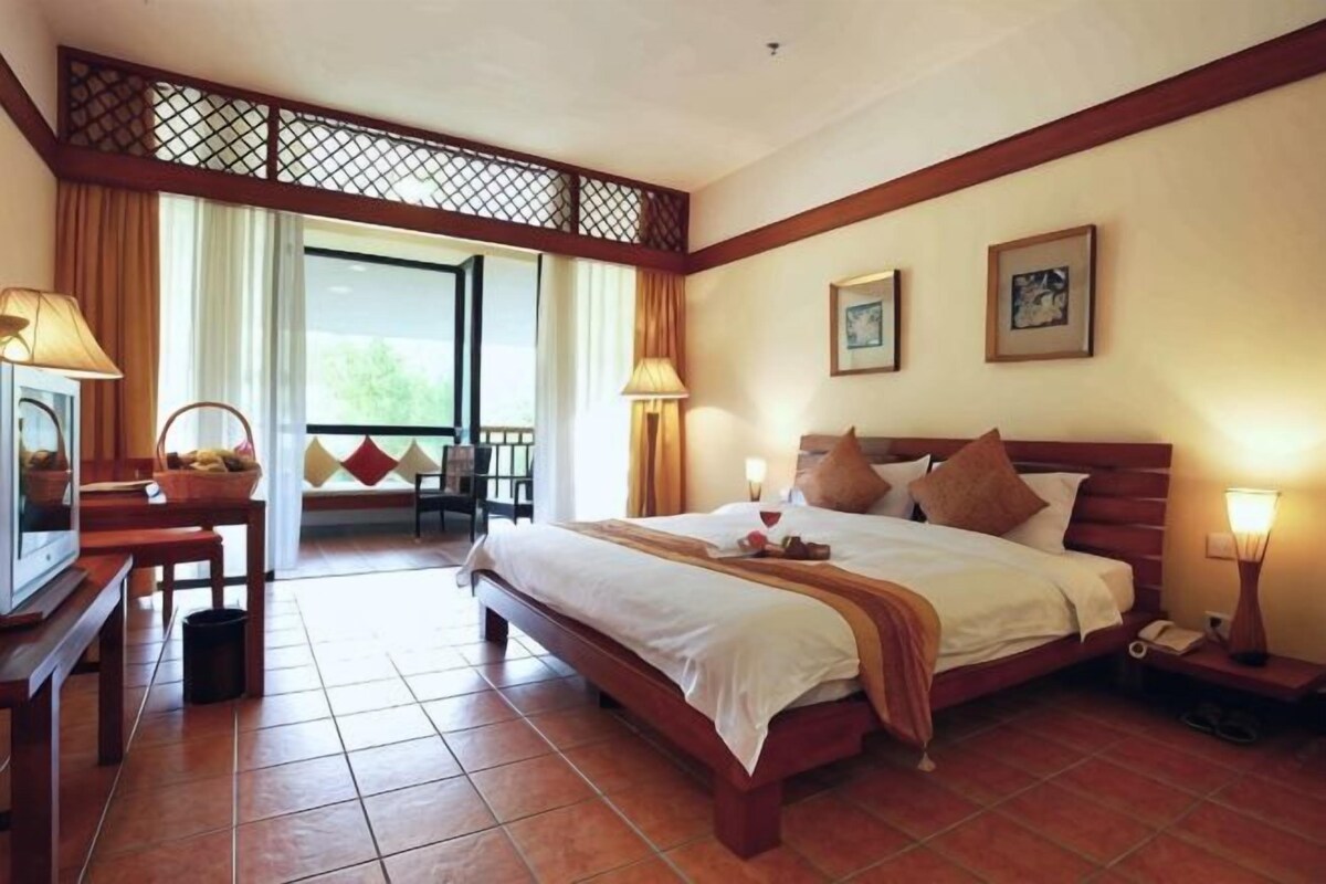 A hotel room with a bed, bedside lamps, a desk with a lamp, a television, and a view of the outdoors.