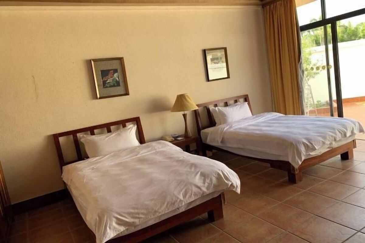 Two single beds with wooden frames and white bedding, a small bedside table with a lamp, and two framed pictures on the wall.