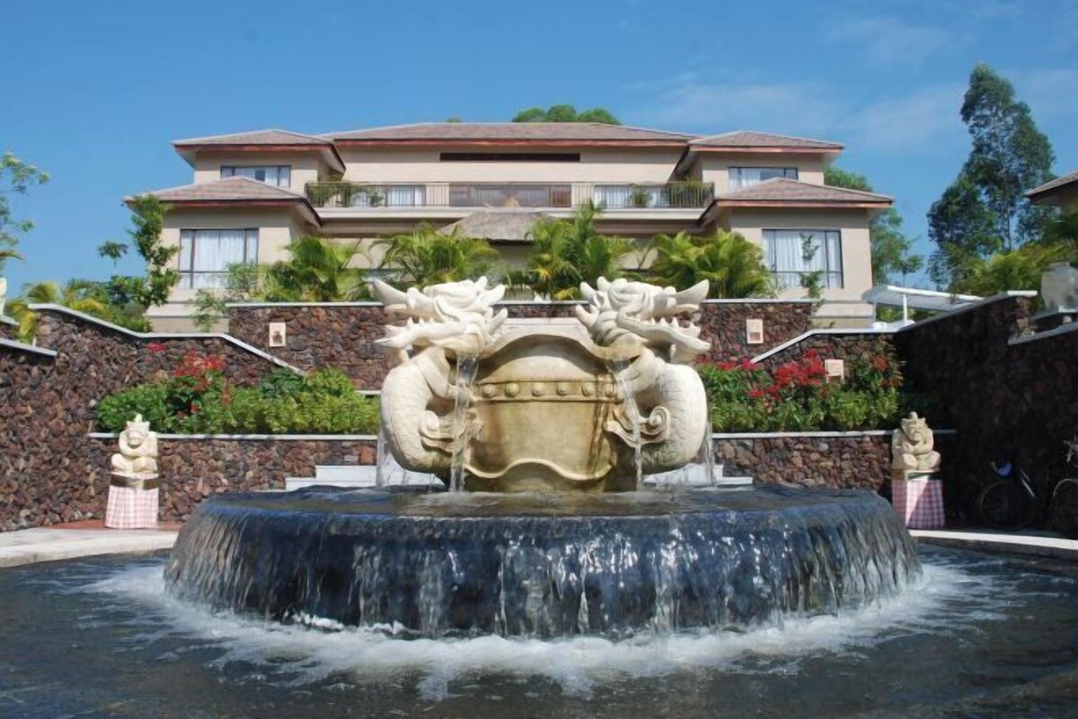 A multi-story building with a stone facade, a central water feature with two dragon statues, and a stone wall with greenery.