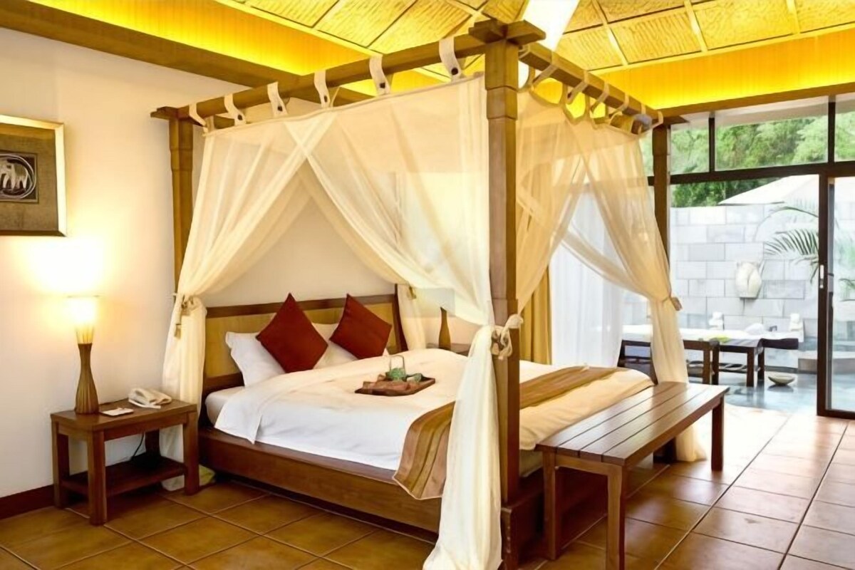 A four-poster bed with a canopy, bedside tables, and a view of the outdoors.