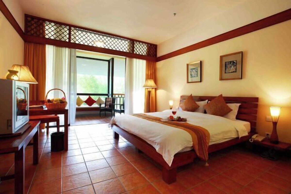 A hotel room with a large bed, two bedside tables, a TV, and a balcony with a view.