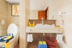Ein Badezimmer mit Toilette, Waschbecken und Spiegel. An der Wand hängt ein Bild von einem Giraffe, und ein Korb mit Handtüchern steht bereit.