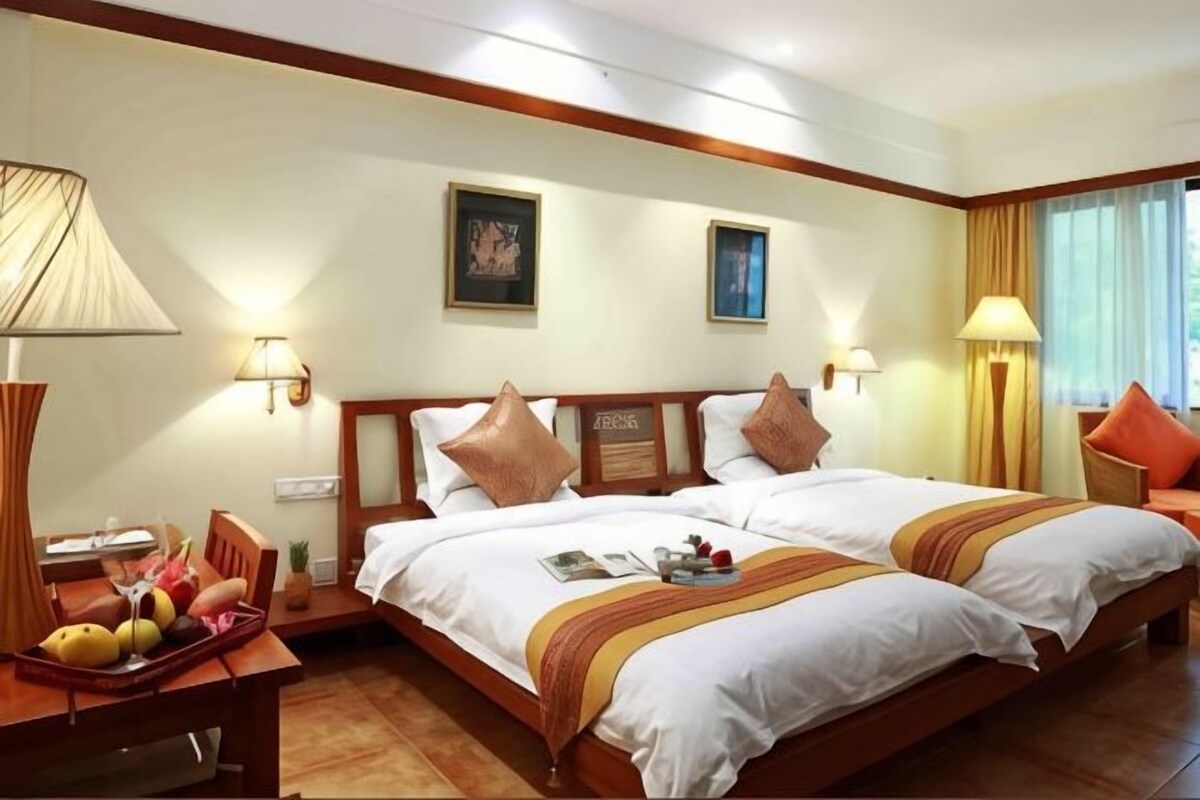 A hotel room with a double bed, bedside tables, lamps, a desk with a chair, and a window with curtains.