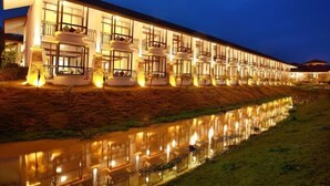 Un hotel moderno con diversi balconi, una piscina a specchio e una facciata ben illuminata.