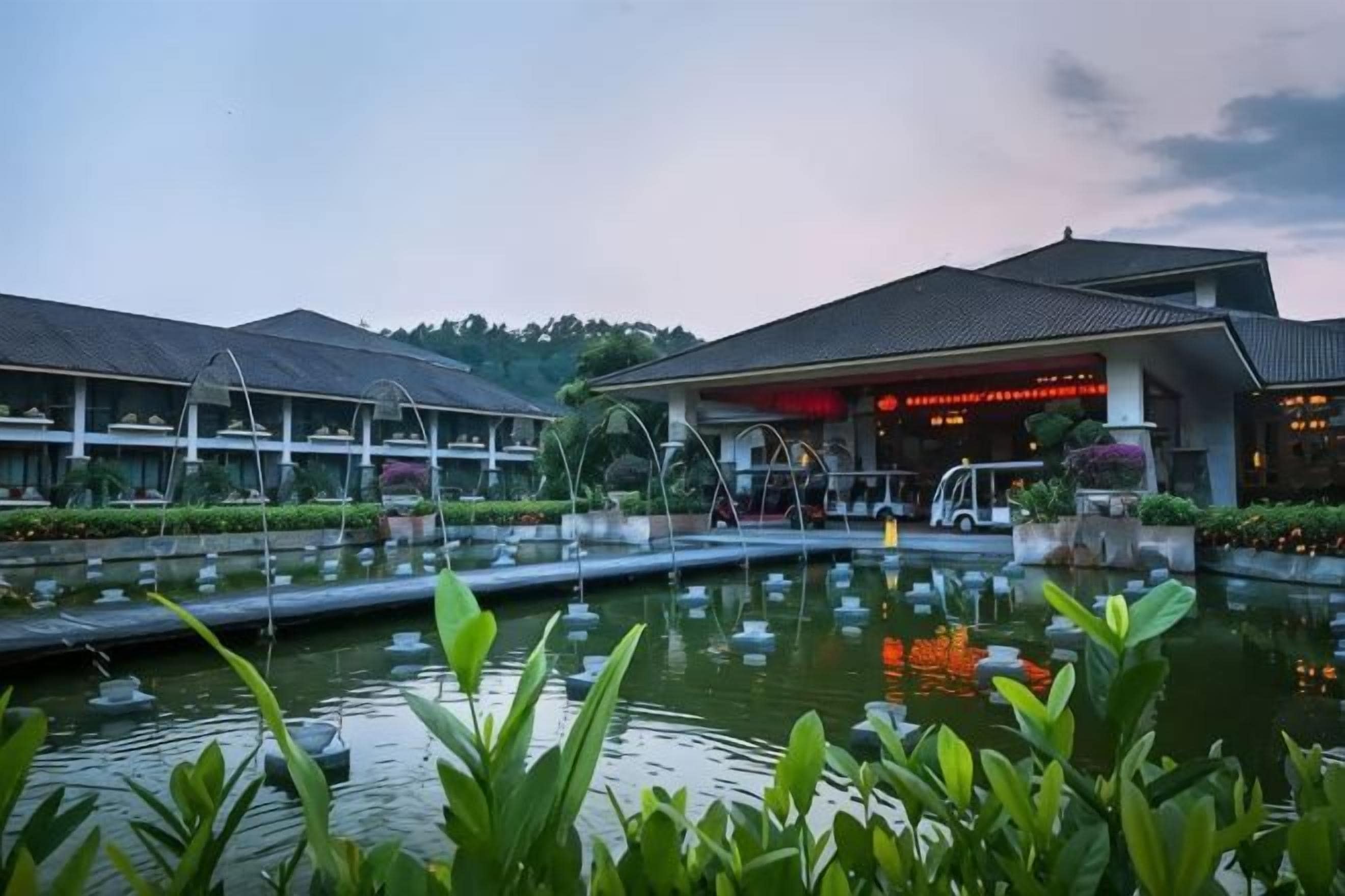 A hotel with a large outdoor pool, a covered walkway, and a building with a red-lit entrance.