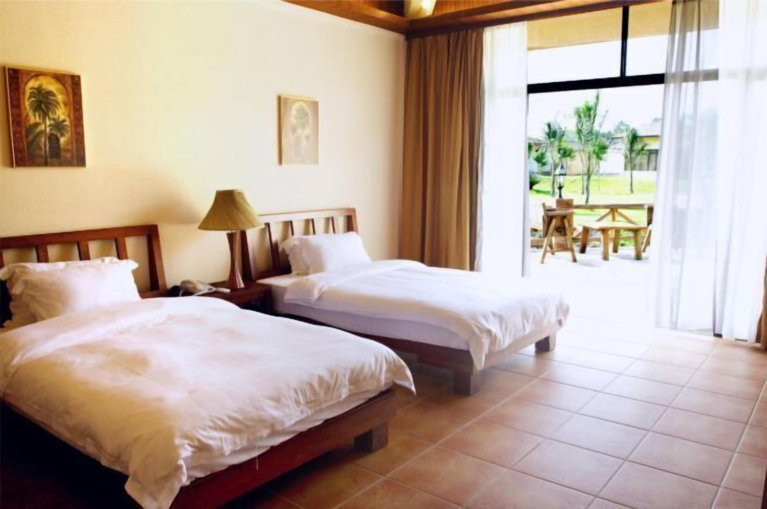 Habitación de hotel con dos camas, una lámpara y vista al patio exterior.