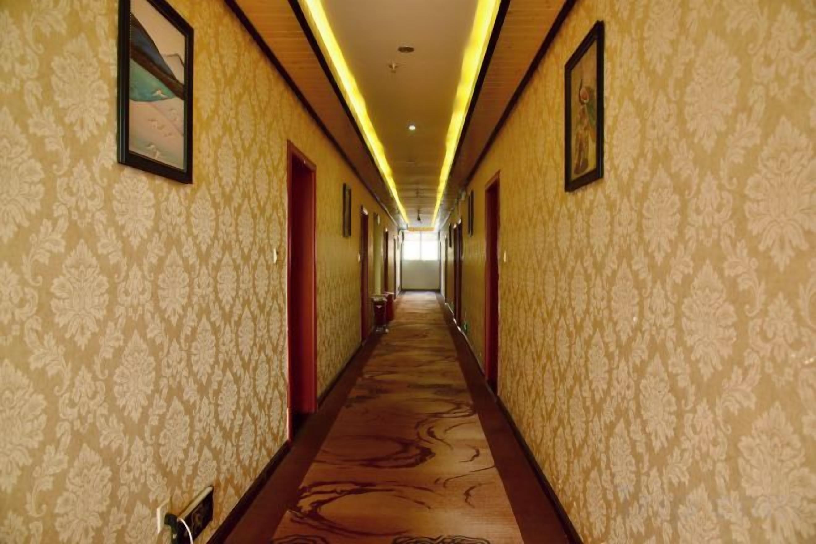 A hotel corridor with patterned wallpaper, doors, and a carpeted floor.