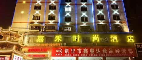Un hôtel à plusieurs étages, avec des fenêtres illuminées et une enseigne bien visible, portant des caractères chinois.