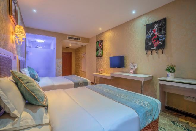 A hotel room with two beds, a desk, a television, and artwork on the walls.