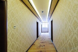 Un couloir étroit, orné d’un papier peint à motifs et d’un tapis à fleurs, qui mène à une pièce lumineuse au fond.