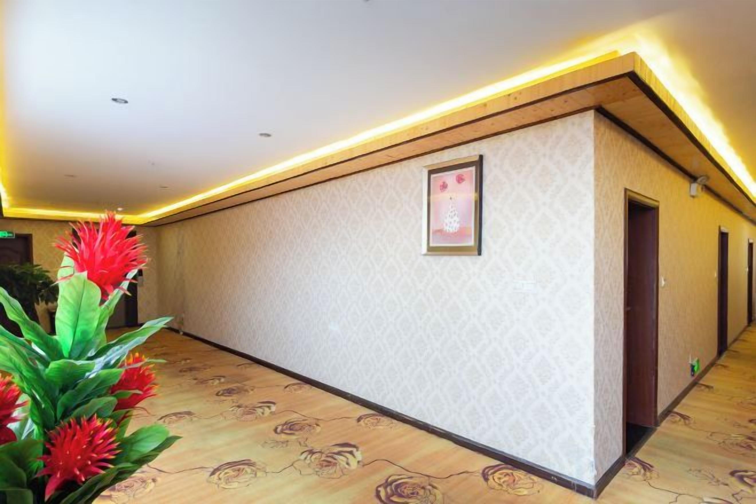 A hotel corridor with patterned walls, a framed picture, and a wooden floor.
