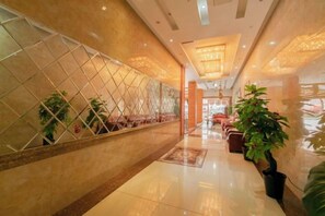 A hotel corridor with a reflective wall, potted plants, and a seating area with chairs. - Kerry Garten Fashion Hotel (Kaili)
