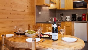 Une table de salle à manger en bois, avec une bouteille de vin, des verres et un bol de raisins.