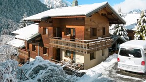 Un chalet en bois doté d’un balcon, entouré de montagnes enneigées.