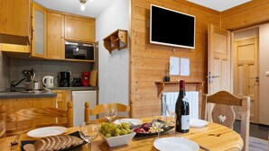 Une cuisine en bois avec une table à manger dressée pour un repas, comprenant une bouteille de vin, un bol de raisins et une assiette de pain tranché.