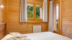 Une pièce aux murs lambrissés, avec un lit, une fenêtre avec des rideaux et un radiateur.