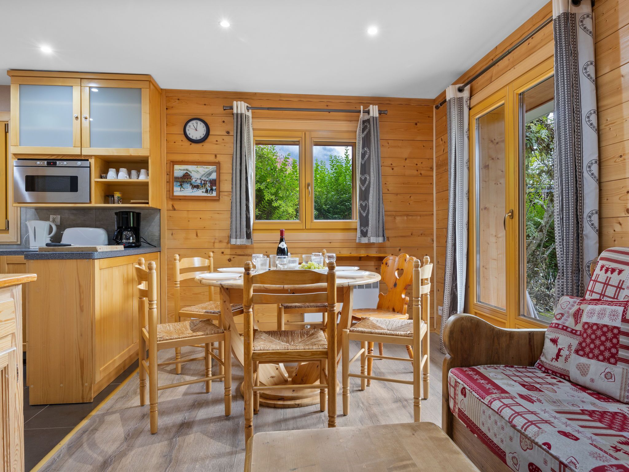 Une pièce confortable, aménagée comme un chalet, avec des murs en bois, une table à manger avec des chaises, un canapé et un coin cuisine équipé d’une horloge et d’une machine à café.