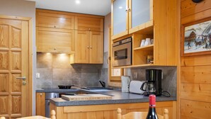 Une cuisine avec des meubles de rangement en bois, une cuisinière, une machine à café et une table à manger, mise avec des verres et des assiettes.