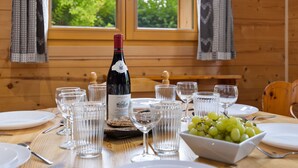 Une table de salle à manger en bois, mise avec des verres à vin, une bouteille de vin et un bol de raisins.