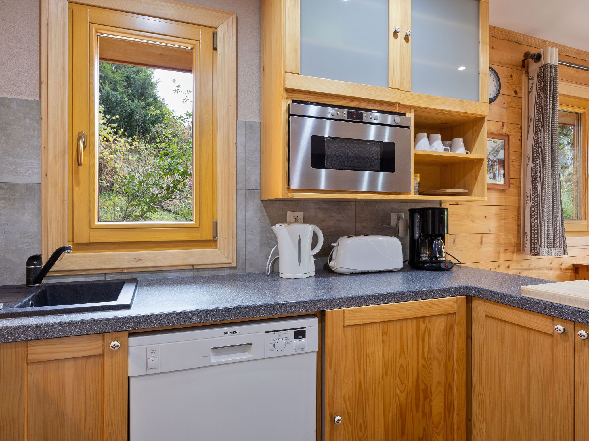 Une cuisine moderne avec des meubles en bois, un four en acier inoxydable, un lave-vaisselle et une machine à café.