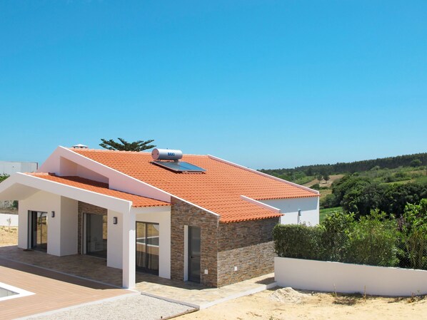 Una casa moderna con un tetto in tegole rosse, un pannello solare e un serbatoio d'acqua.