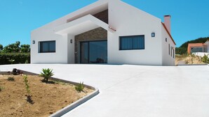 Una casa moderna de dos pisos con techo plano, ventanas grandes y entrada de hormigón.