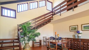 Un comedor amplio con una escalera de madera, una planta grande en maceta y una mesa de comedor con sillas.