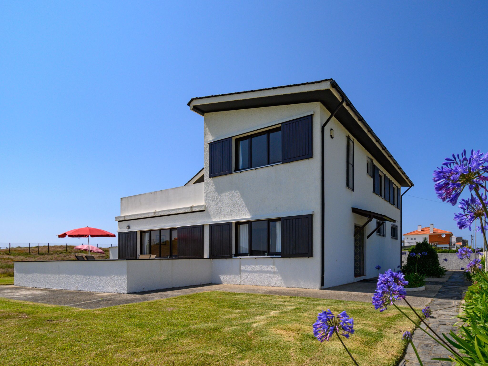 Ein modernes, zweistöckiges Haus mit flachem Dach, großen Fenstern und einem gepflegten Rasen.