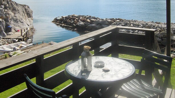 A lakeside patio with a table and chairs, a small boat docked nearby, and a view of the lake and mountains. - Hardangerrorbu by Interhome (Tjoflot)