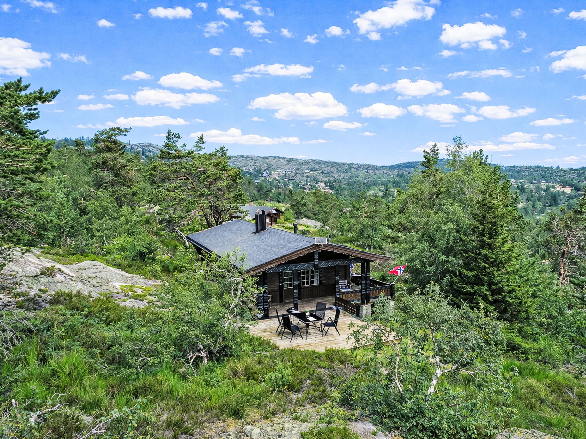 A cabin with a deck, surrounded by dense forest and mountains in the background.